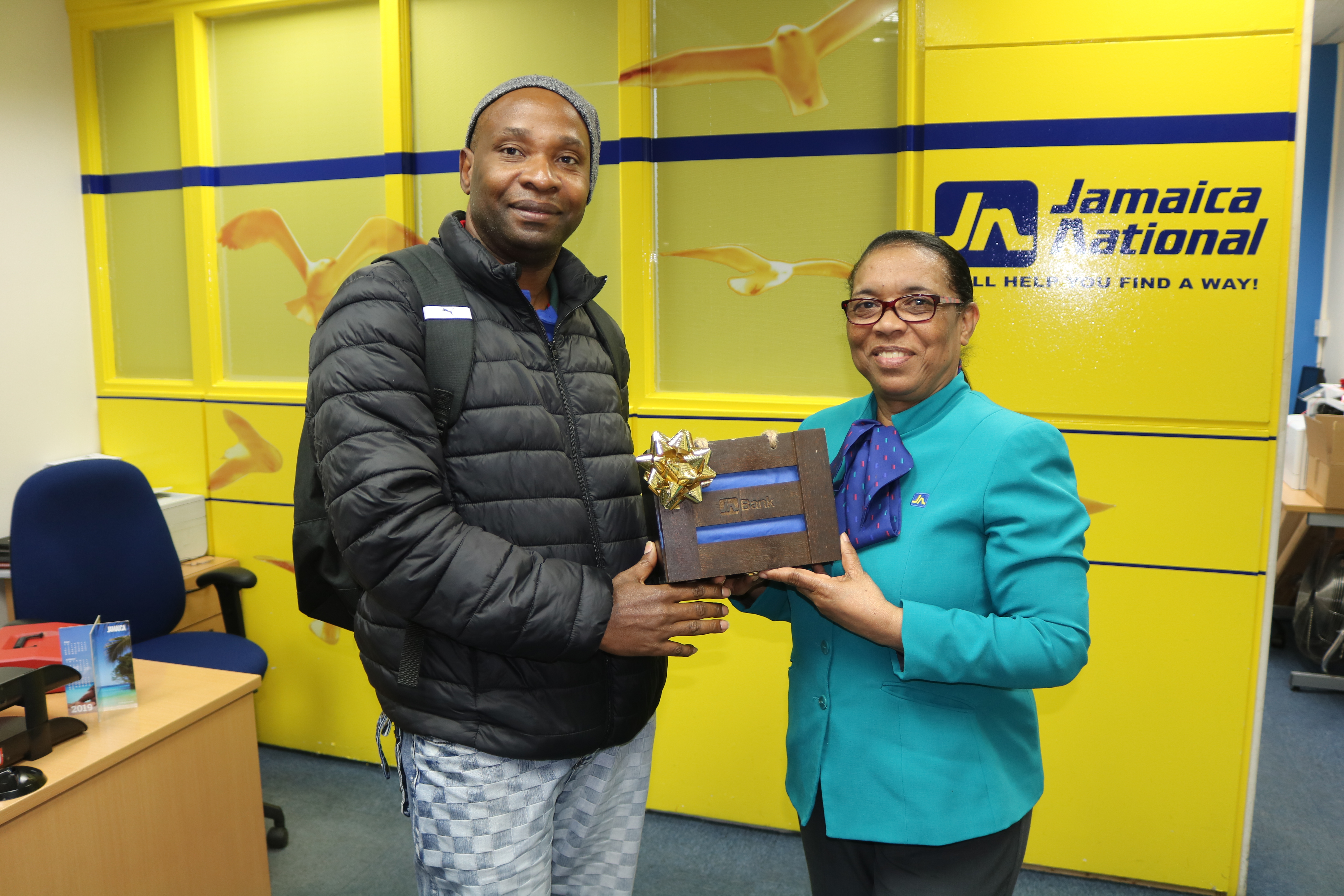 Arnett Pryce (right), member service representative, JN Bank UK Representative Office presents Stanhope Gibbs, a JN member with a “Braata box” as part of the organisation’s “Celebrate our Jamaican Heritage Promotion”. Mr Gibbs received an authentic token that was made by a social enterprise in Jamaica for opening a JN Bank Savings Account .