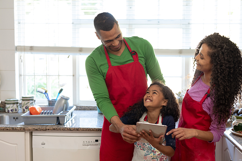Front view of a mixed race couple with their daughter in a kitchen at Christmas, using a laptop computer - JN Bank