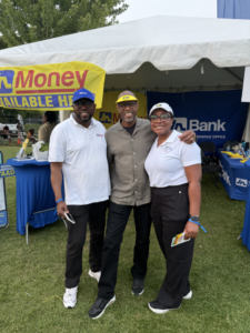 20260810_001733625_iOS - JN Bank Three people stand together outdoors at a booth under a white tent, smiling for the camera with bank banners in the background.
